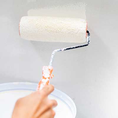 Close up of a hand painting an interior wall white with a large paint roll