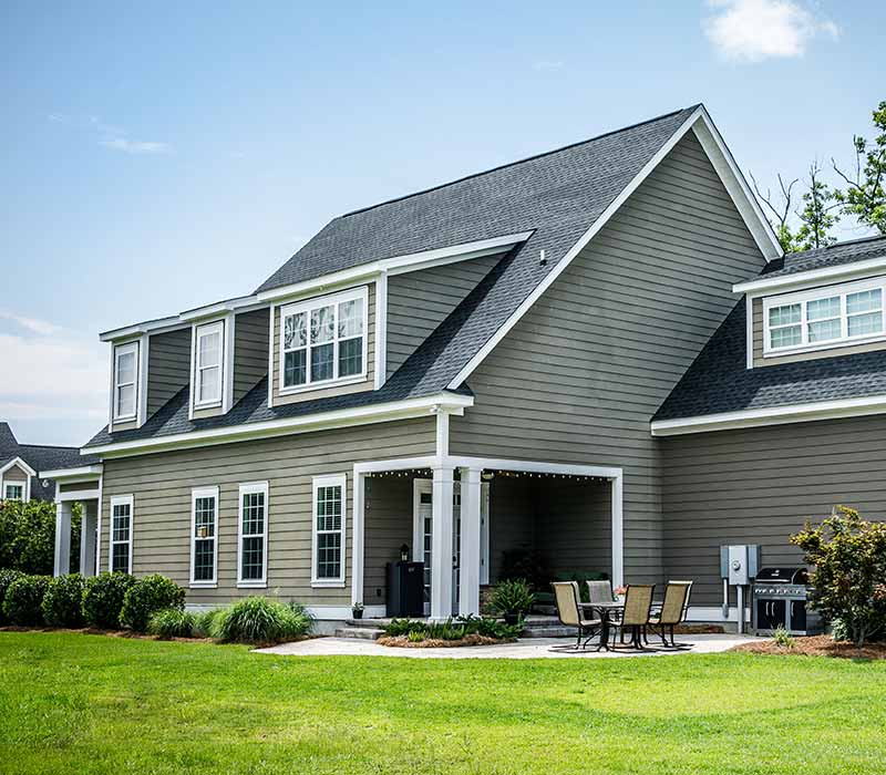 Backyard of a gray, mid-class home with a small outdoor patio area and a gray shingle roof
